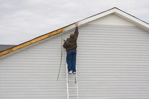 man on ladder repairing damage to home